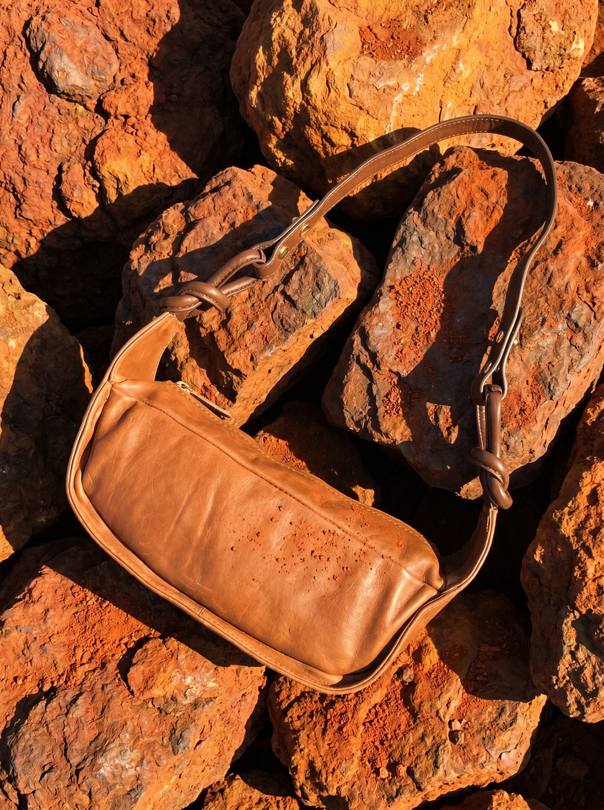 Pilbara Knot chocolate leather bag resting on red Pilbara rocks
