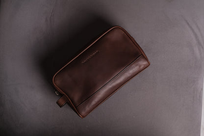 Upside view of brown leather toiletry bag kept on a woolen bed in shady scene.