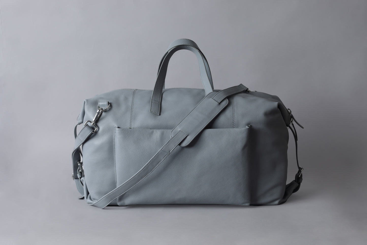 a light grey leather duffle bag placed against a grey background.