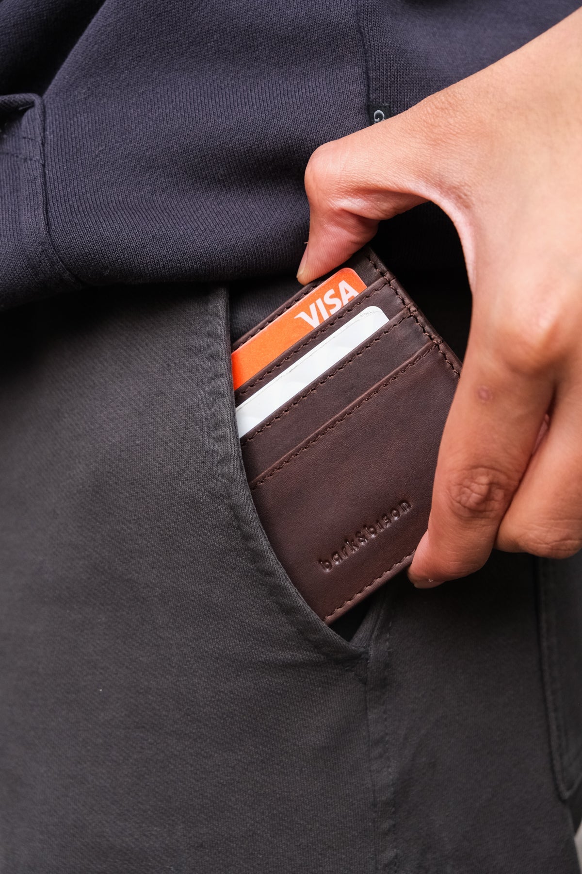 close up of man taking out of left pocket leather cardholder embossed with bark&bison