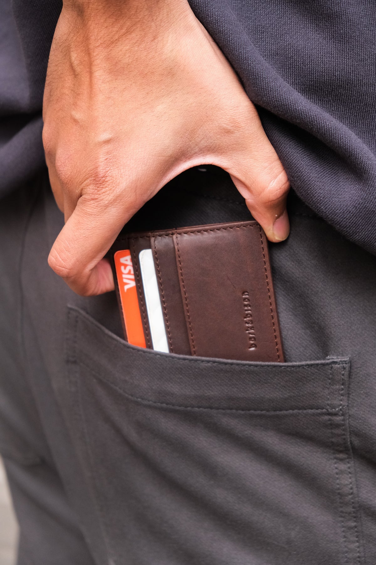 close up of man taking out of back pocket leather cardholder embossed with bark&bison