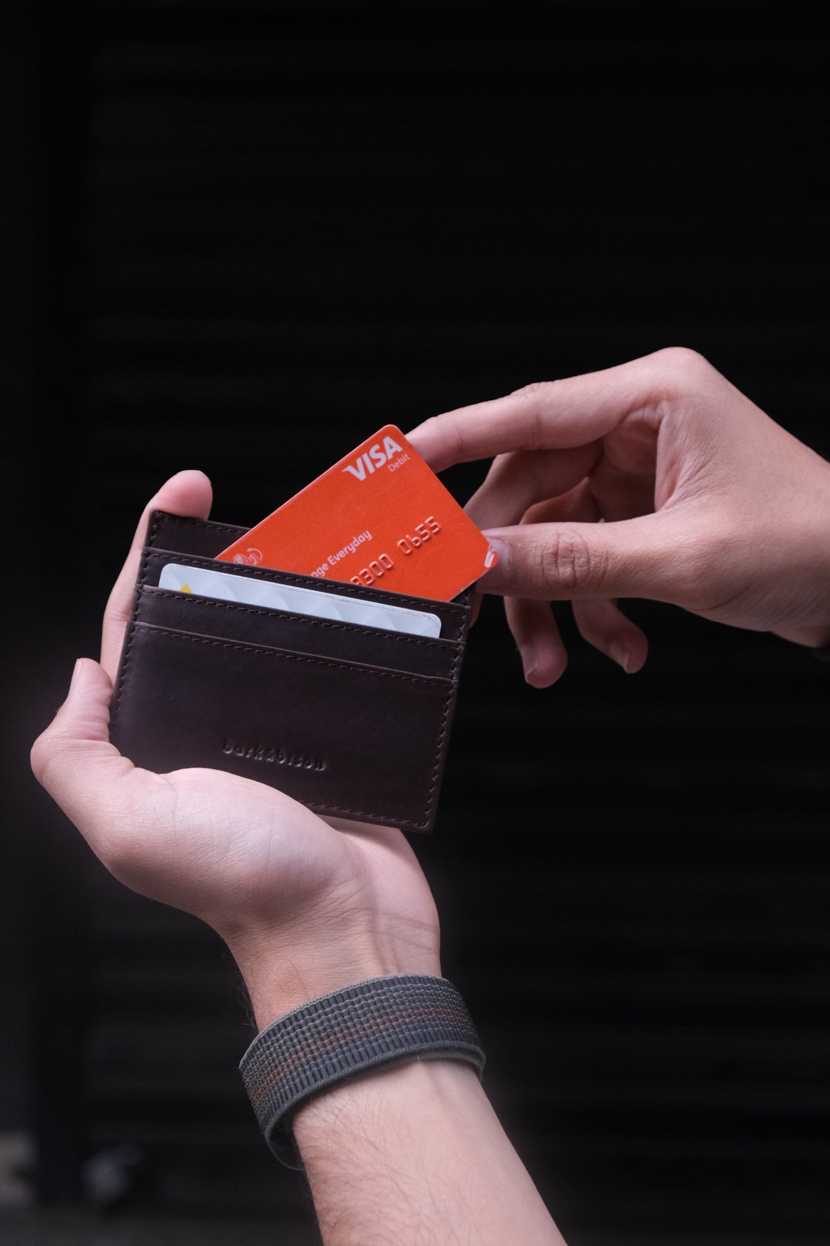 man's hand taking credit card out of the leather brown cardholder of bark&bison against black background