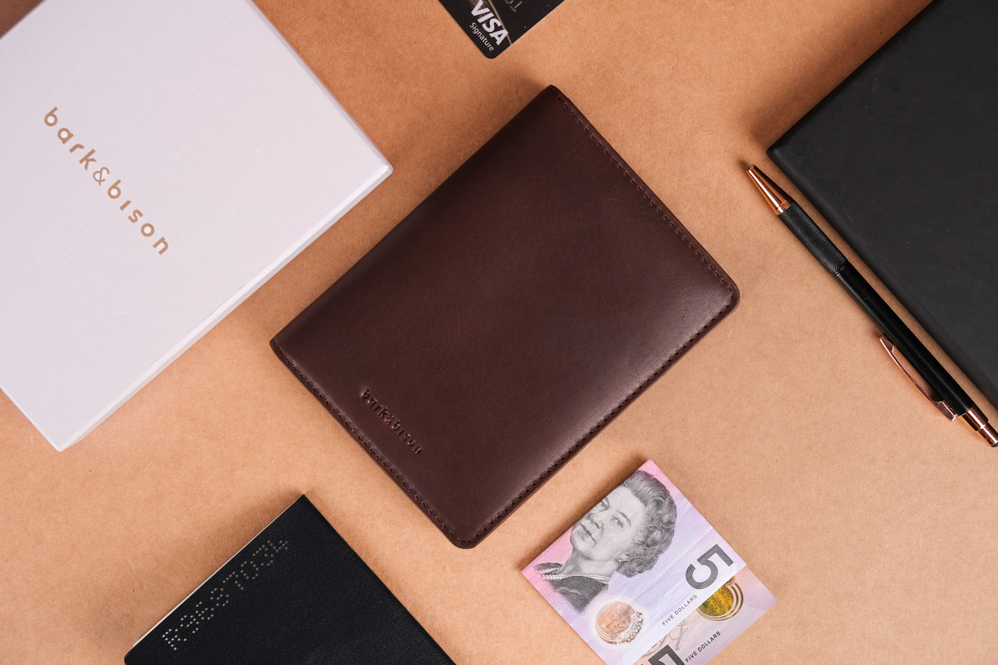 a dark brown leather wallet with bark&bison branding next to a currency note and white paper with bark&bison branding.