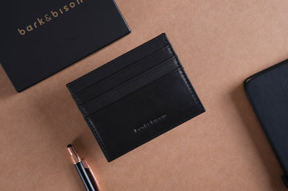 A black leather card wallet embossed with "bark&bison" and a black box also embossed with "bark&bison" against a brown background