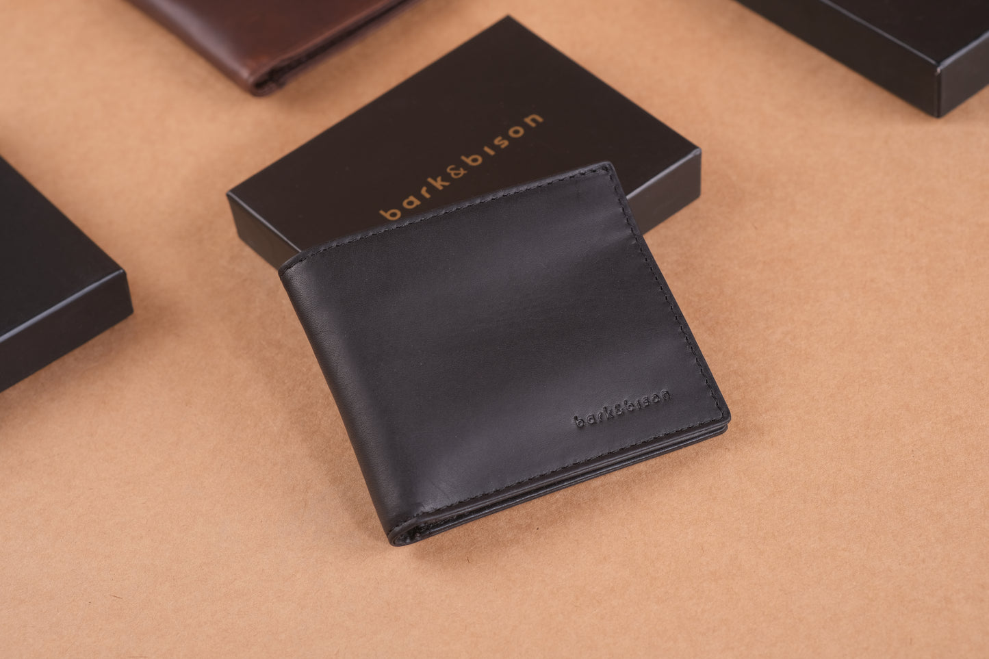 A black leather wallet is placed on a brown surface with bark&bison boxes in the background.