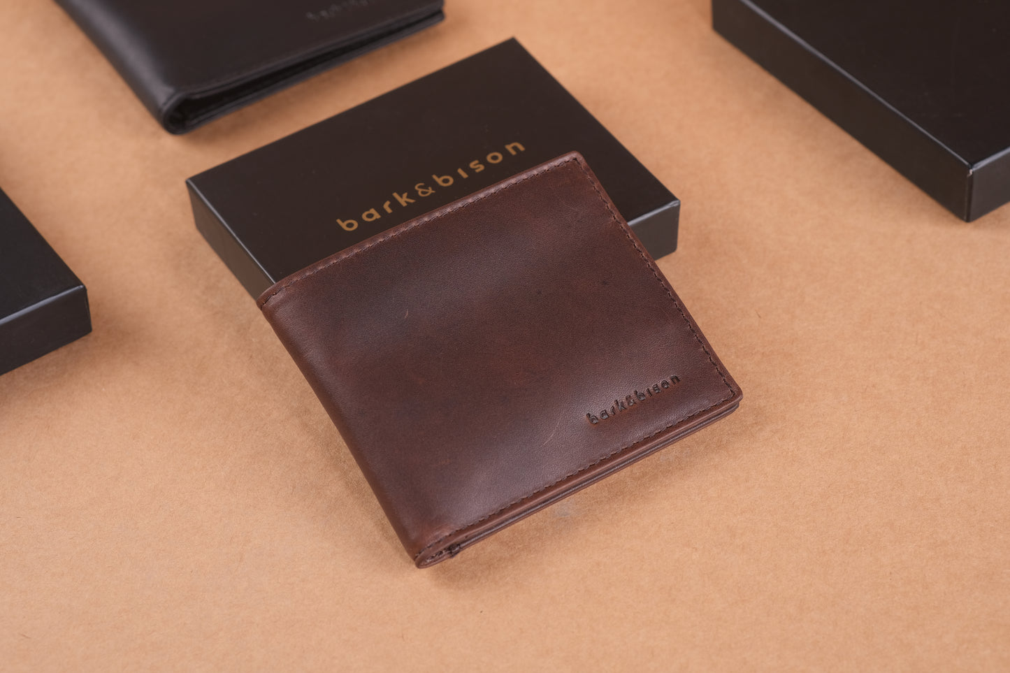 A brown leather wallet is placed on a brown surface with bark &amp; bison boxes in the background.