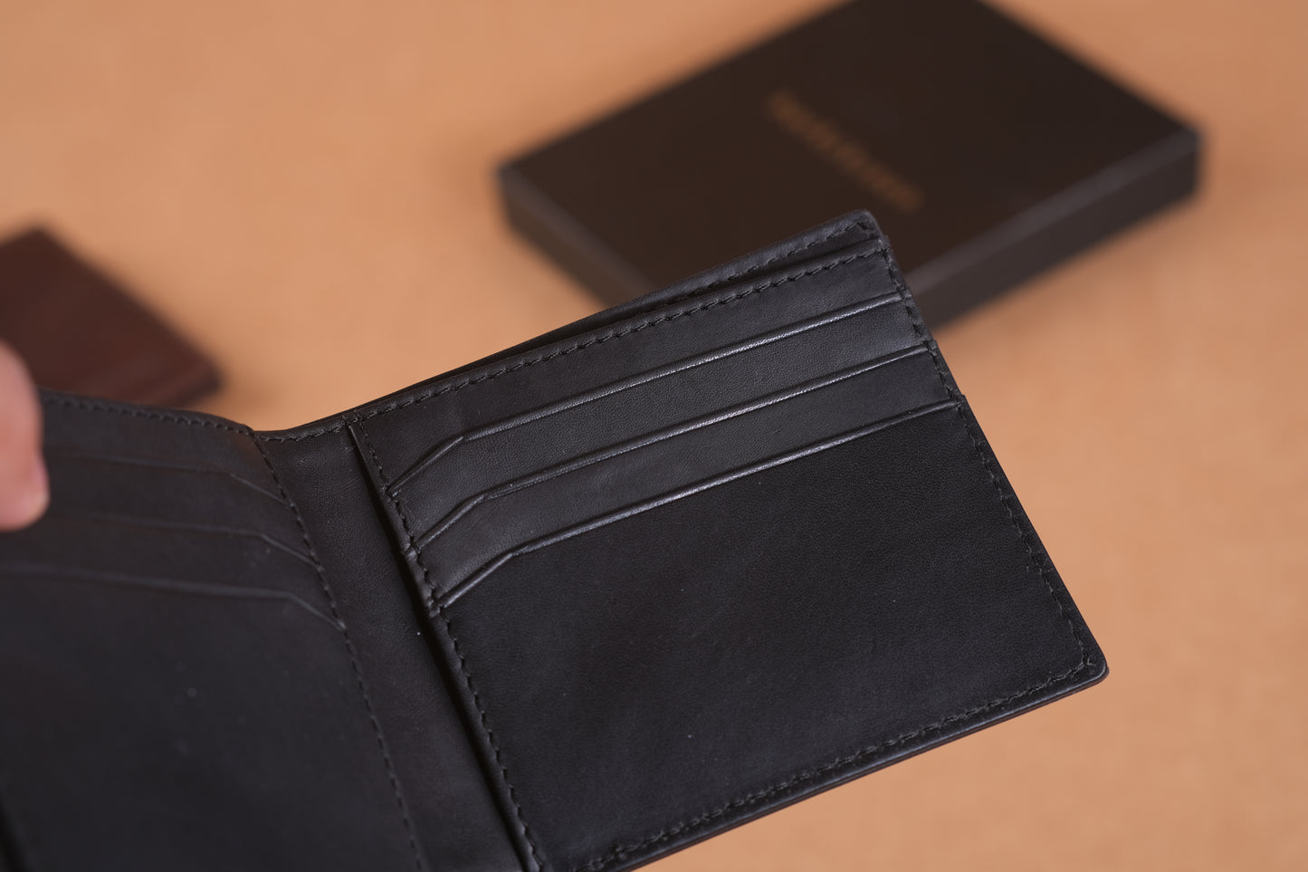 A black leather wallet with multiple card slots is open, set against a blurred brown background.