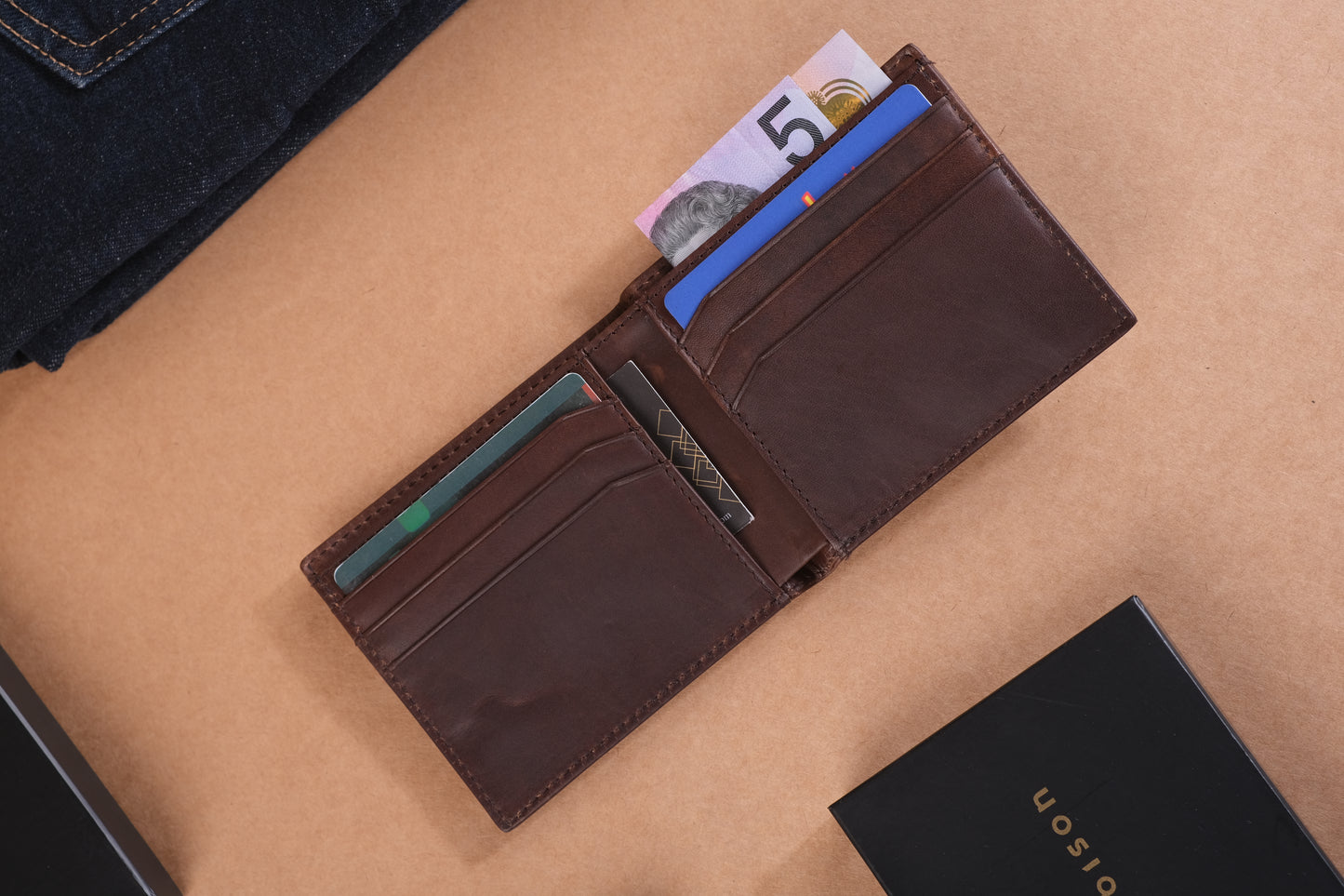 Open dark brown leather wallet with banknotes and multiple cards visible on a brown surface with bark&bison branding.