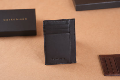 A black leather cardholder with several slots is displayed upright on a brown surface next to a black box with bark&bison branding.