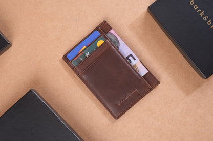 A brown leather wallet holding credit cards and cash is placed on a brown surface, surrounded by black boxes with bark&bison branding.