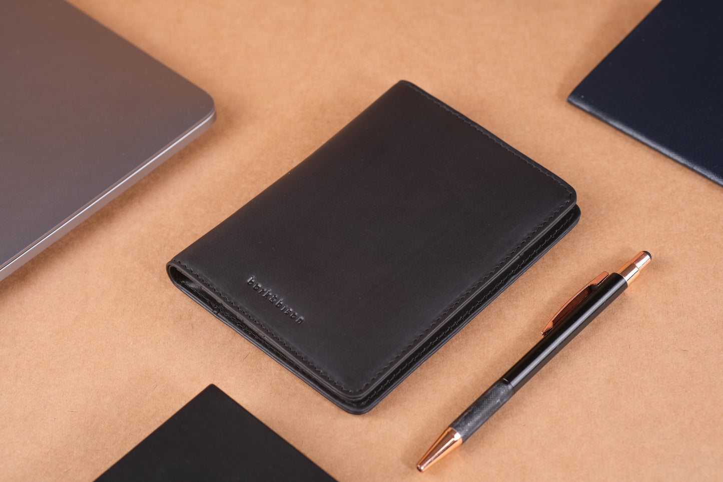 a black leather wallet with bark&bison branding next to a black pen against a brown background.