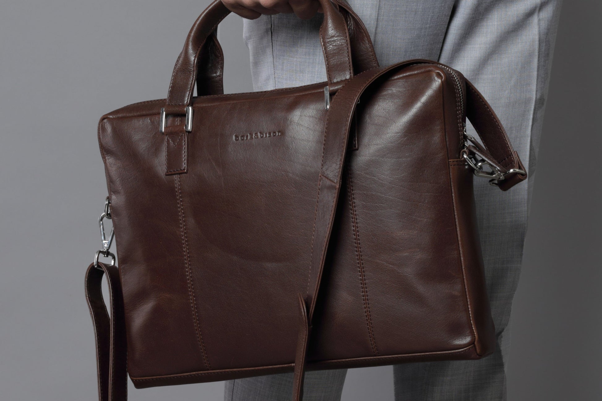 close up of man holding a dark brown leather handbag embossed with bark&bison