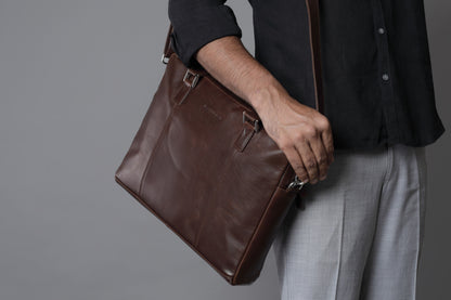 close up of man holding shoulder leather bag of bark&bison against a grey background