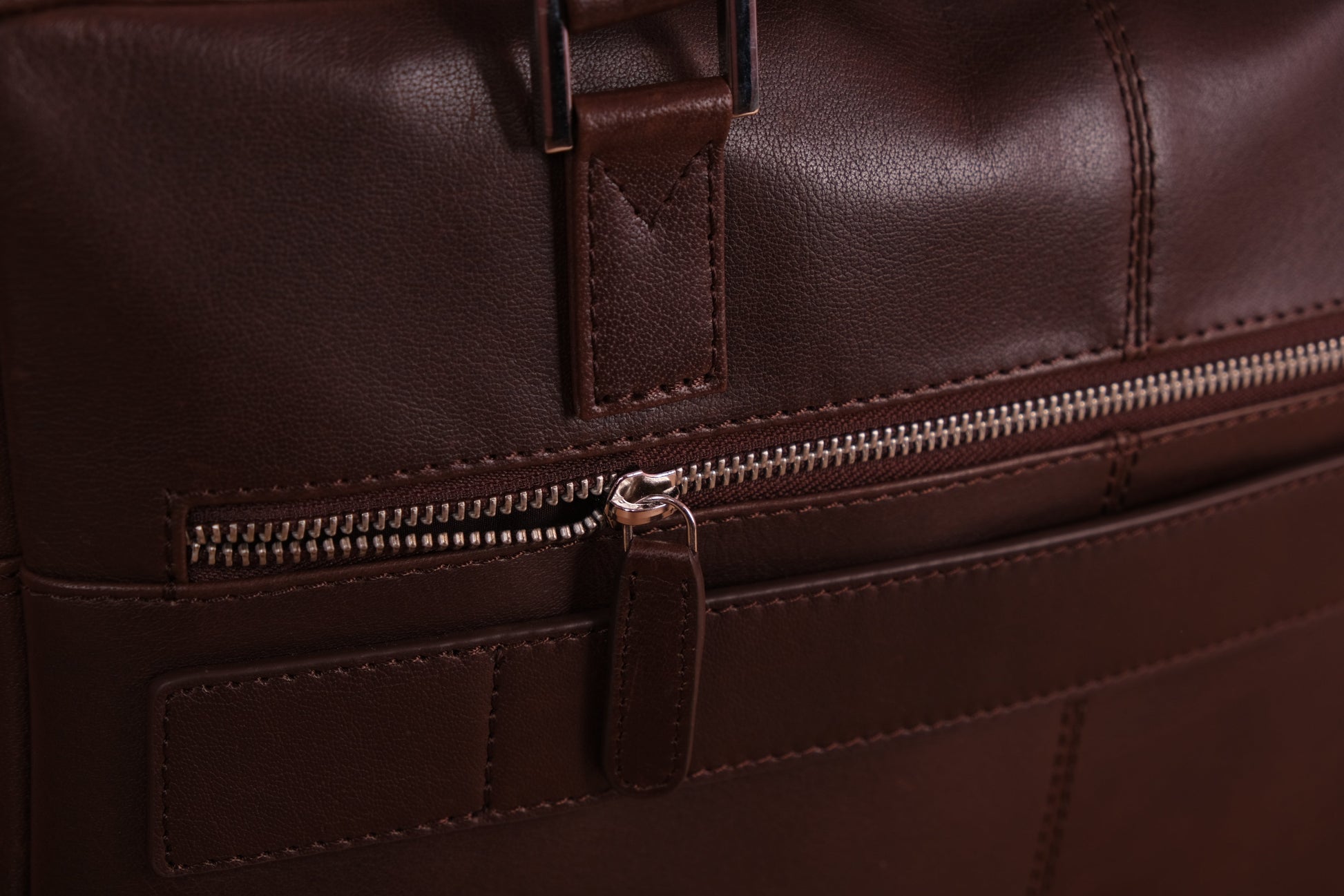 Front close up of dark brown leather handbag showing zip and front pocket.