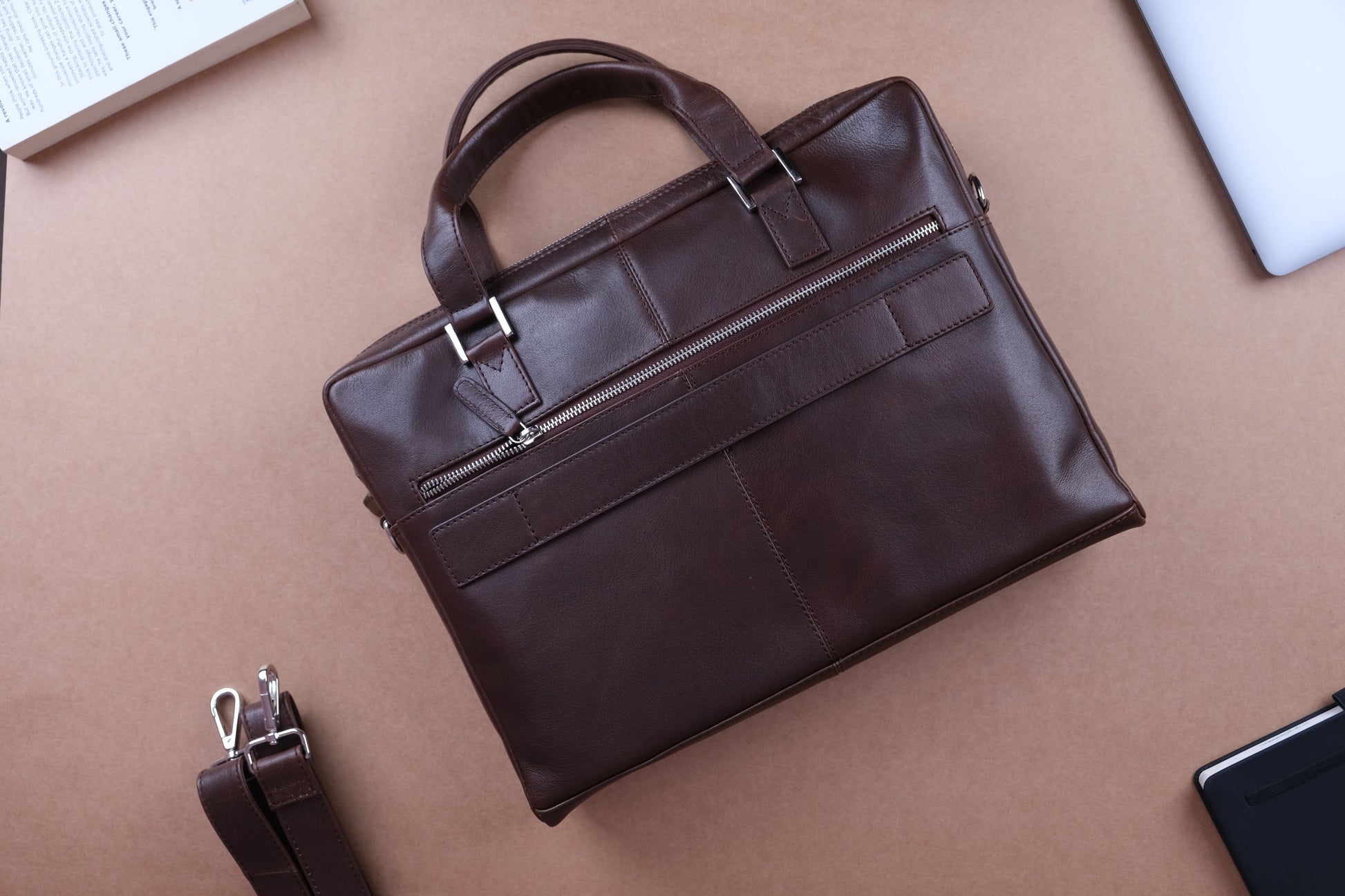 A dark brown leather handbag with detachable shoulder strap against a brown background.