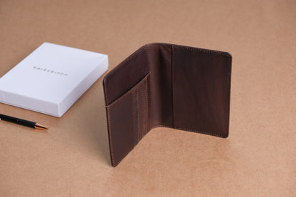 Brown leather wallet with multiple card slots, displayed open on a beige surface. A white box with "bark&bison" branding and a black pen with gold accents are placed nearby.