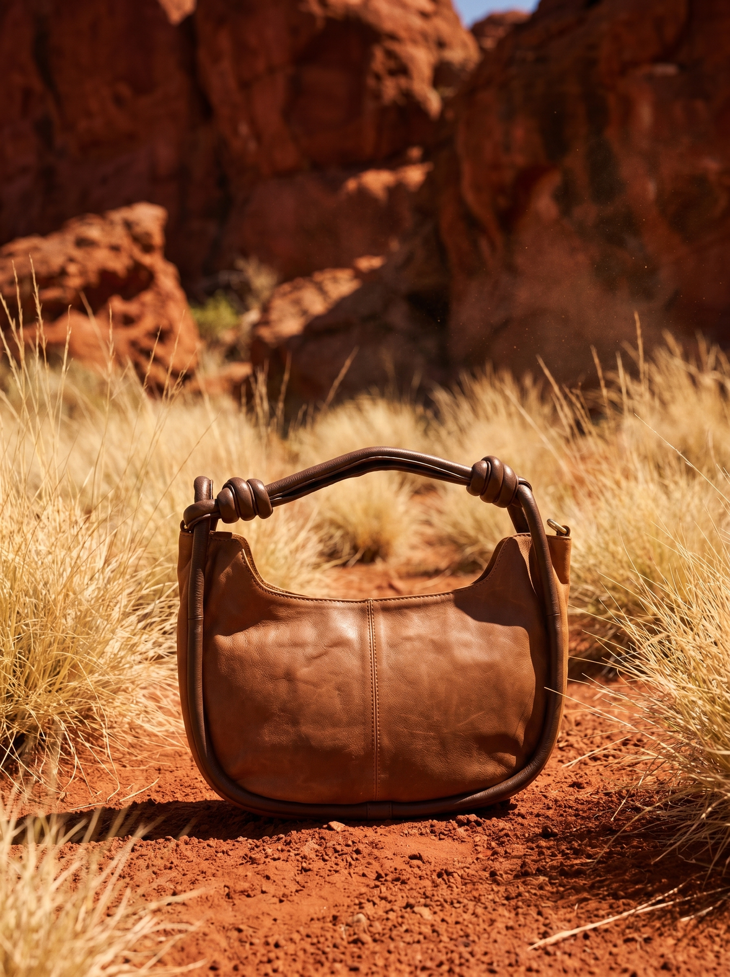 Pilbara Crescent tan leather hobo bag resting on red rocks with spinifex grass