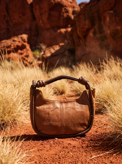 Pilbara Crescent tan leather hobo bag resting on red rocks with spinifex grass