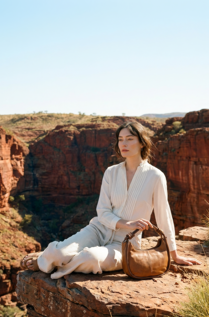 Model sitting on red rocks with a dog and the Pilbara Crescent bag in a desert gorge setting