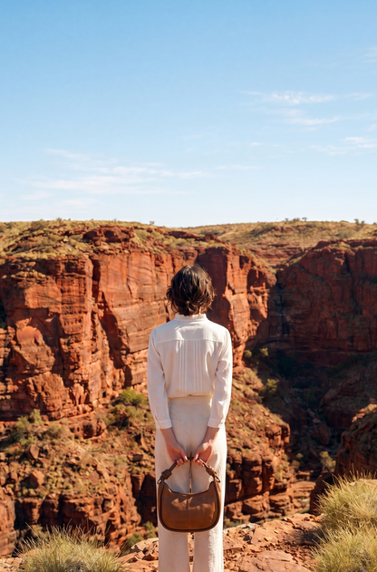 Model viewed from behind at the edge of a red gorge, holding the Pilbara Crescent bag