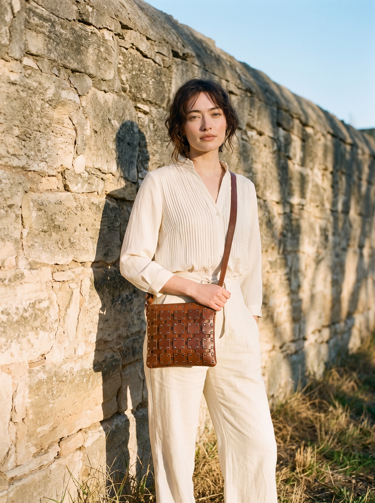 Model wearing the Gawler Sling crossbody bag against a heritage stone wall, woven basketweave panel visible