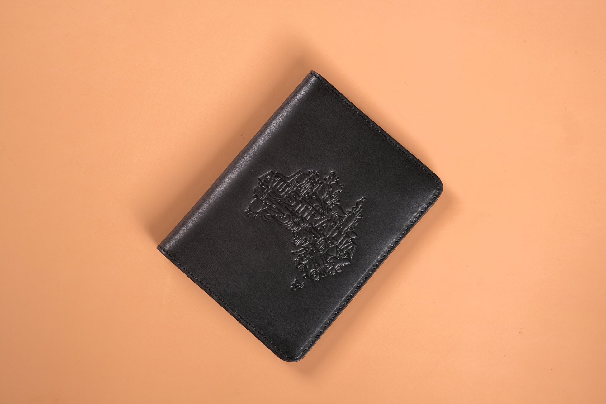 A black leather passport holder embossed with the Australian coat of arms and the word "AUSTRALIA," against a light tan background.