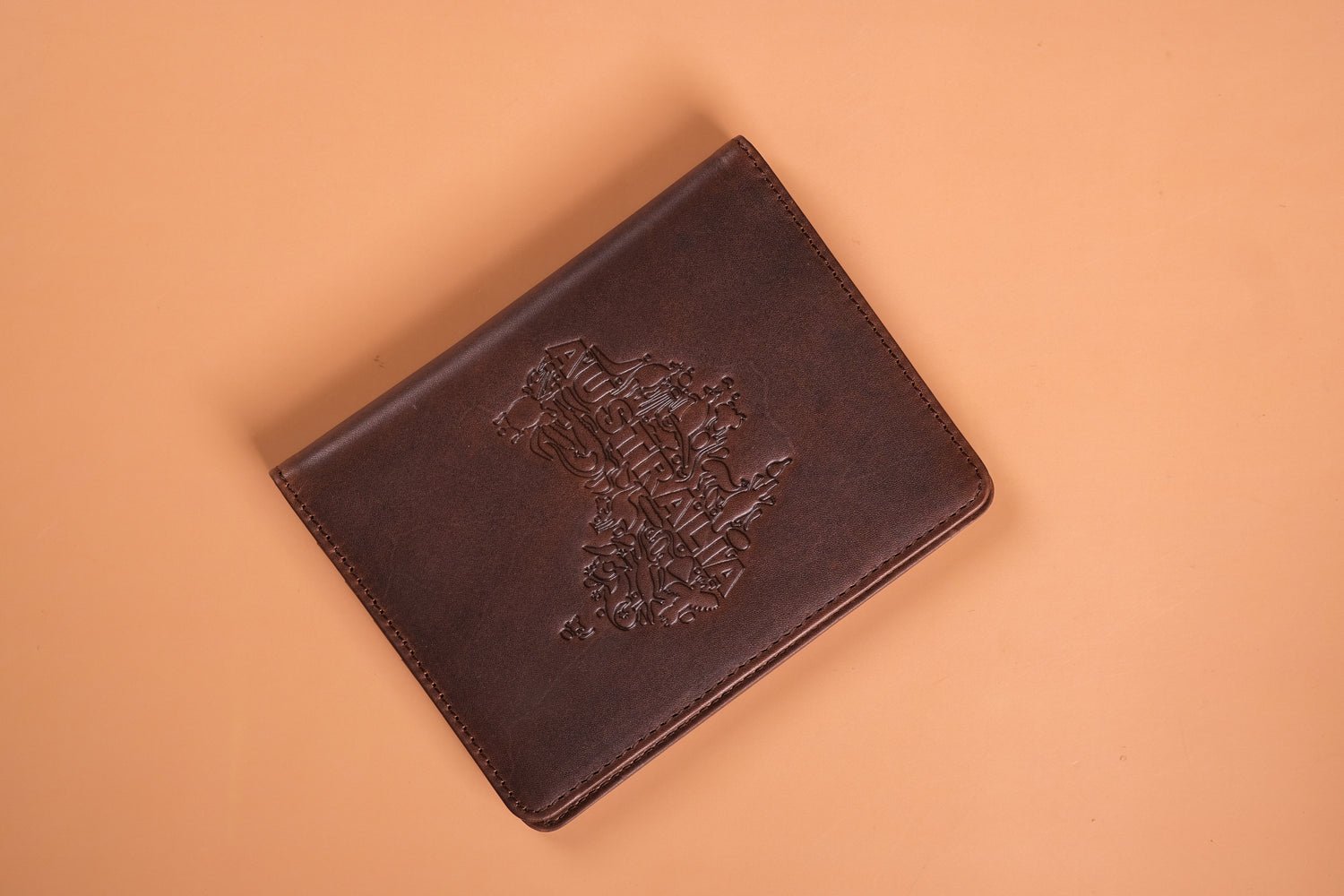 A brown leather passport holder embossed with the Australian coat of arms and the word "AUSTRALIA," against a light tan background.