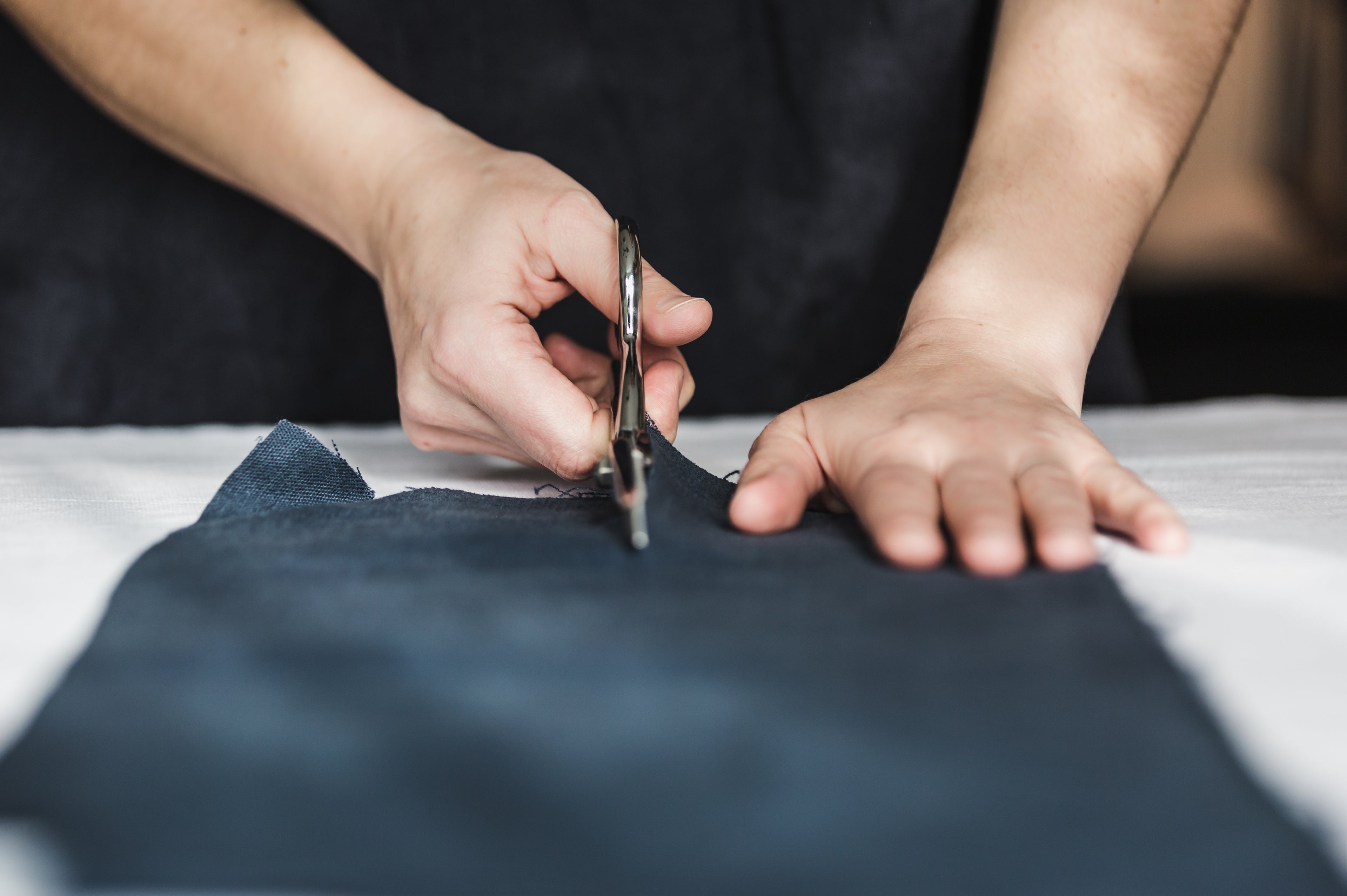 Close-up of hands cutting dark fabric with scissors on a flat surface, showcasing precision in tailoring or crafting.